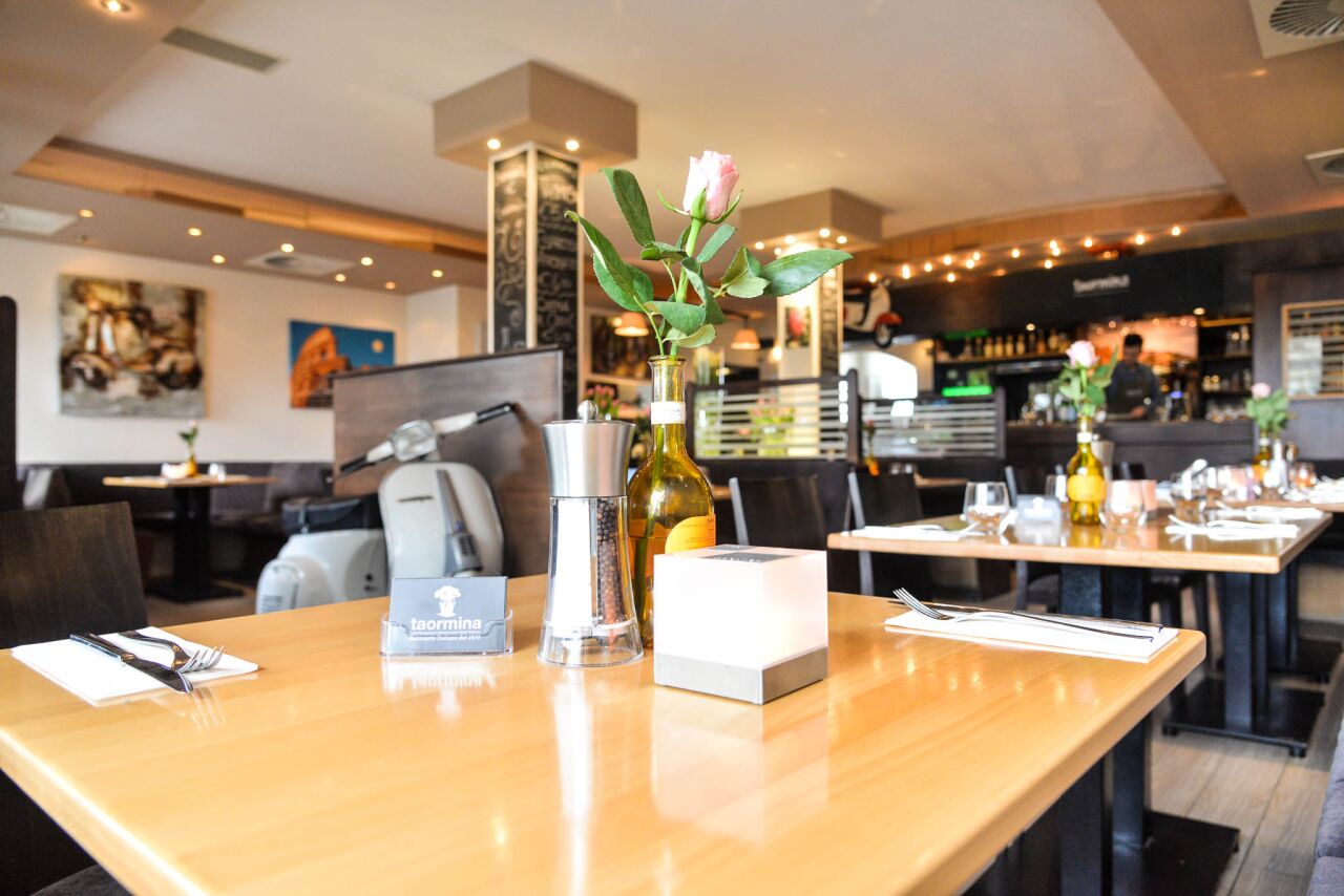 Gedeckter Holztisch mit Pfeffermühle und Olivenöl, dahinter eine Vespa und die Bar