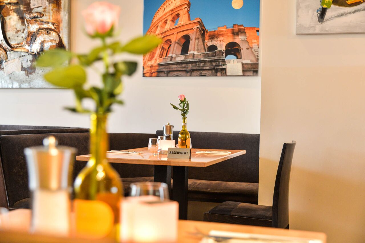 Rose in an olive oil bottle on the table, a picture of the Colosseum on the wall