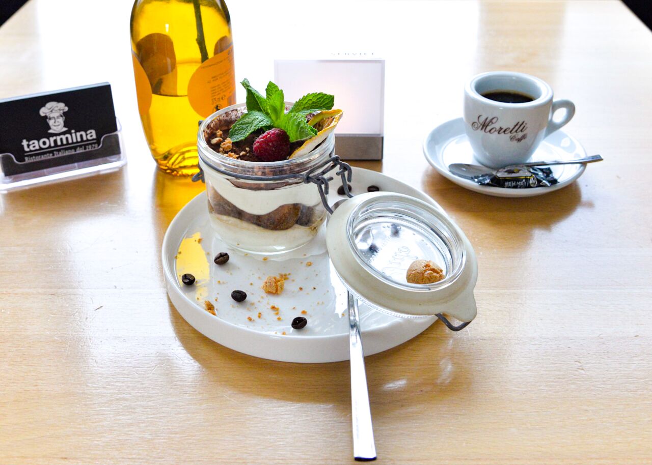 Tiramisu im Glas mit Minze und Beeren, daneben ein Espresso und eine Flasche Likör